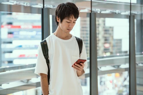 キャンパスの建物前でスマートフォンを見る男子学生