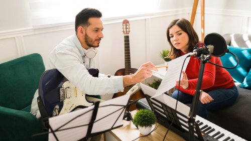 ギターを持つ男性と楽譜を見ながら音楽制作をする女性
