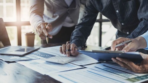電卓やノートパソコンを使い、会計データを分析しながら打ち合わせをするビジネスパーソンたち