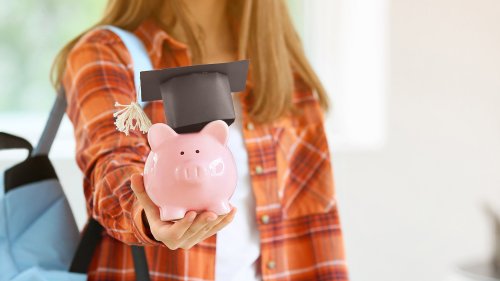 学位帽をかぶり貯金箱を手にした学生(学費と奨学金のイメージ)
