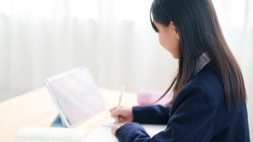 机の上で書類とノートパソコンを見比べながら確認する学生